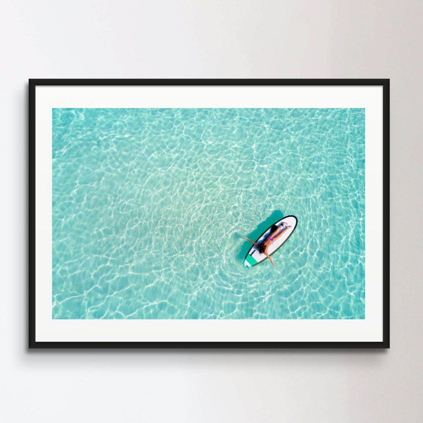 Aerial view of a woman on a surfboard in the turquoise waters