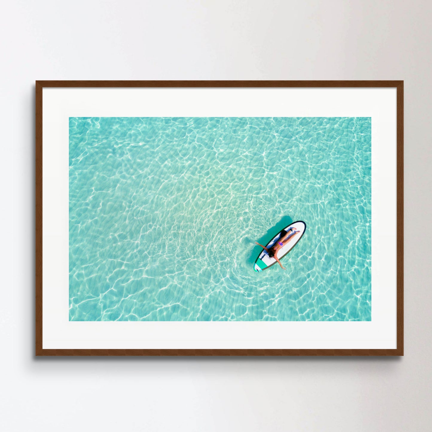 Aerial view of a woman on a surfboard in the turquoise waters