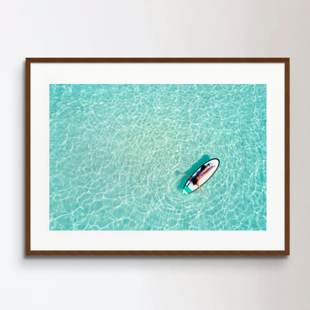 Aerial view of a woman on a surfboard in the turquoise waters